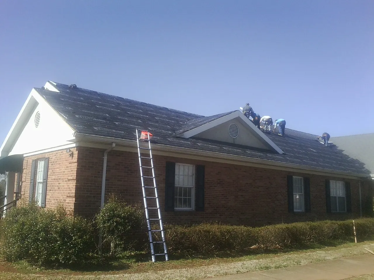 Crew tearing shingles off a brick ranch roof with a ladder set — Metal Roof Repair work by our crew in Worthington