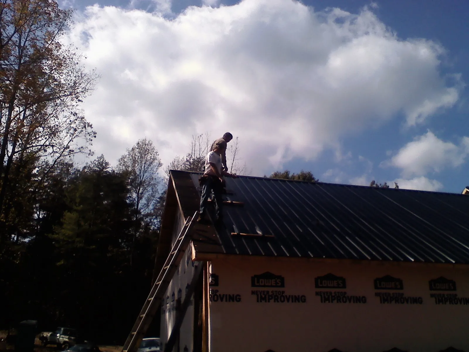 Roofer fastening dark metal panels high against a cloudy sky, from a Roof Inspection job in Worthington