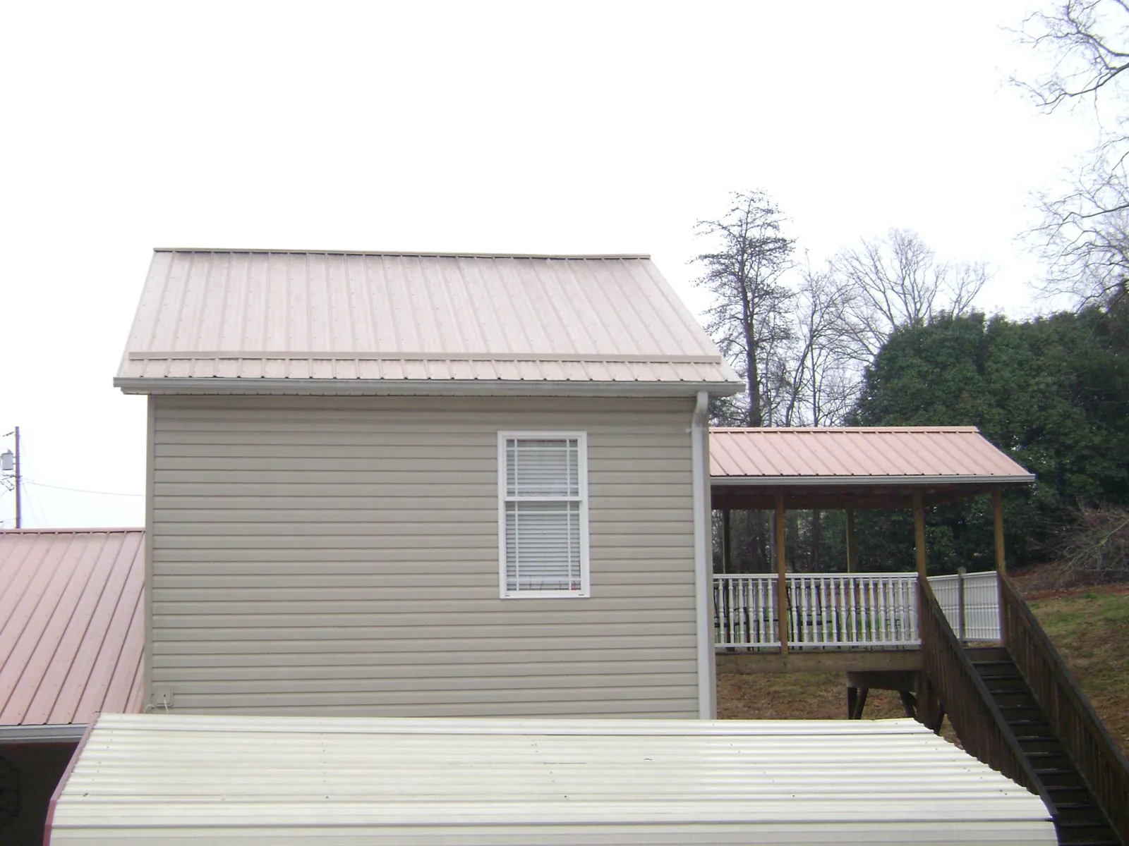 Tan metal roofs on a two story addition and attached porch, from a Roof Replacement job in Worthington