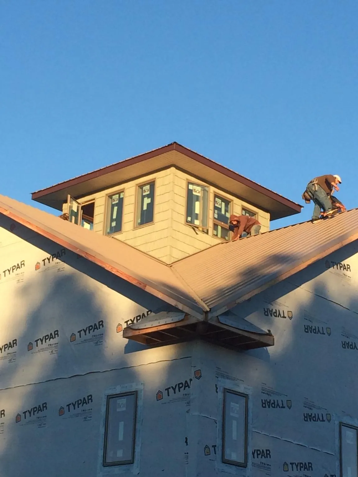 Roofers working around a rooftop cupola on a new metal roof at sunset in Worthington